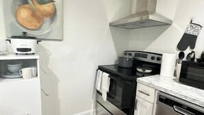 Eine kleine Küche mit weißen Schränken, einem Edelstahlbackofen, einer Mikrowelle und einem Geschirrspüler. An der Wand hängt ein Gemälde mit Früchten und der Boden ist aus Holz.