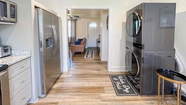 A modern kitchen with stainless steel appliances, a wooden floor, and a view into the living area.