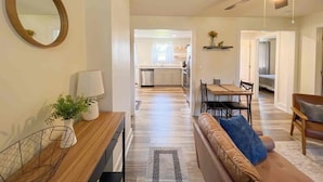 A modern living room with a sofa, a dining table, and a kitchen in the background.