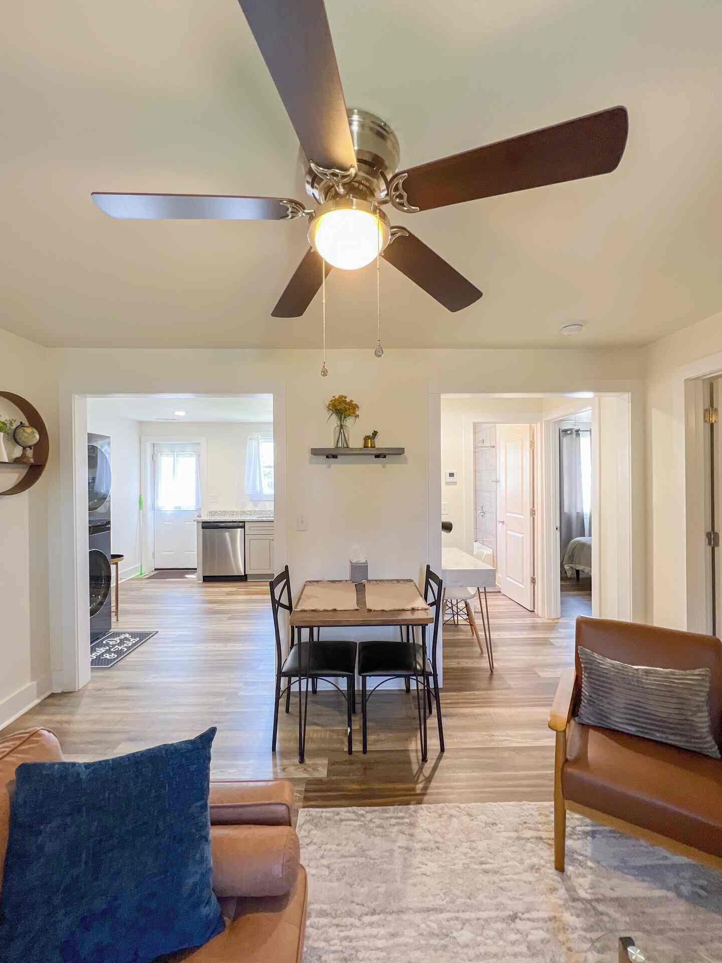 Un vaste espace de vie doté d’un ventilateur de plafond, d’une table à manger avec des chaises, d’un canapé et d’une cuisine à l’arrière-plan.