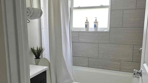 A bathroom with a bathtub, toilet, and a window above the sink.
