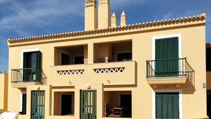 Un edificio de dos pisos con fachada amarilla, contraventanas verdes y tejado de tejas.