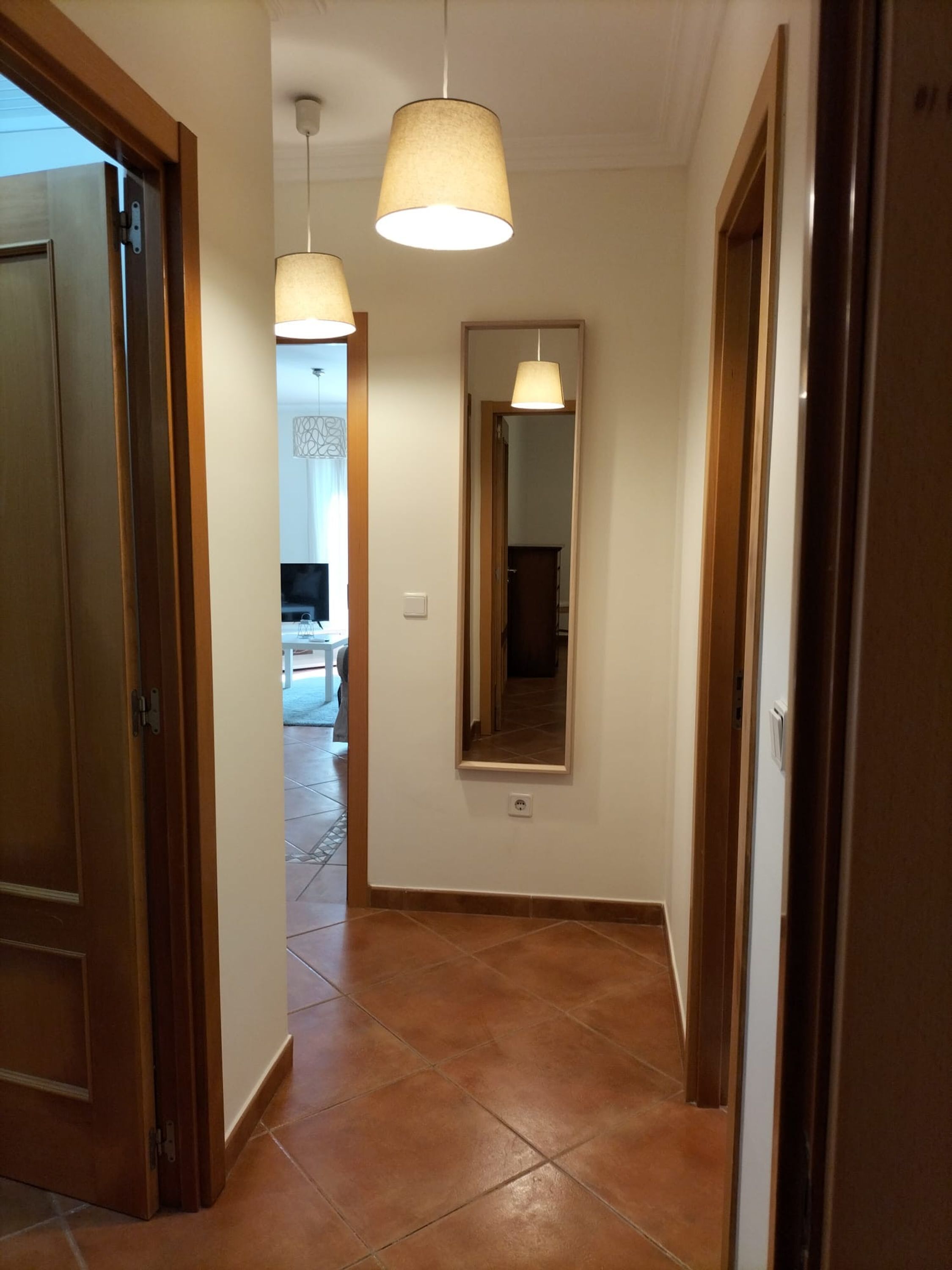 A hallway with wooden doors, a tiled floor, and pendant lighting.