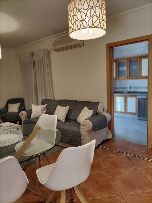 A modern living room with a grey sofa, white chairs, a glass coffee table, and a patterned pendant light. - T2 Vila Bairos A C Piscina e Garagem Vilamoura (Loulé)