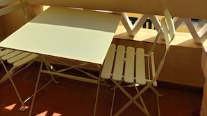 Un patio con una mesa y sillas, barandilla y vistas a palmeras y edificios al fondo.