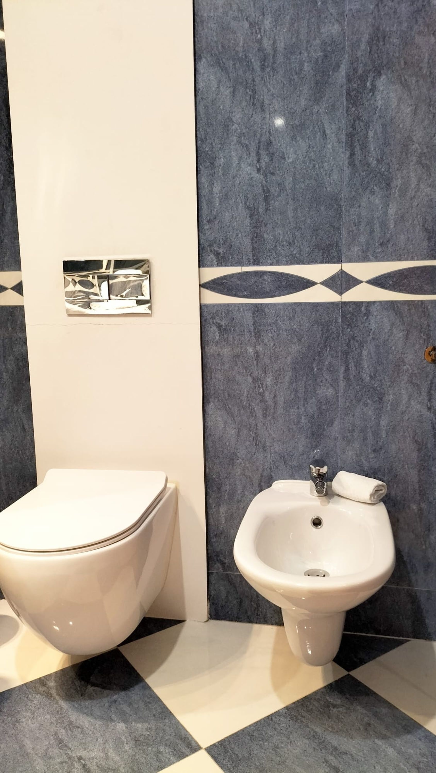 Une salle de bain avec des toilettes et un bidet. Les murs sont recouverts de carreaux disposés selon un motif géométrique.