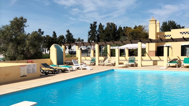 Una piscina con sillas de descanso y sombrillas, rodeada por un edificio con una torre.