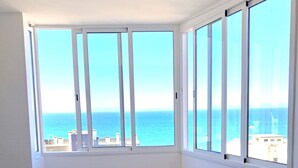 A room with a white table and chairs, large windows with a view of the sea, and wooden flooring. - T1 Pontemira 7C Vista Mar A C 80m Praia (Loulé)