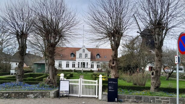 A historic building with a red-tiled roof, surrounded by a white fence and trees. - Apartments in the heart of Hojer (Højer)