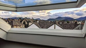 Vue depuis une lucarne sur une ville aux bâtiments traditionnels, avec des montagnes en arrière-plan.