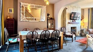 Un espace repas comprenant une longue table et des chaises, une cheminée, un téléviseur fixé au mur et un escalier menant à un autre niveau.