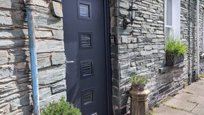 Un bâtiment en pierre avec une porte sombre, une fenêtre et deux plantes en pot placées au sol.