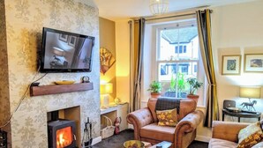Un salon chaleureux avec une cheminée, un canapé en cuir et un téléviseur fixé au mur.