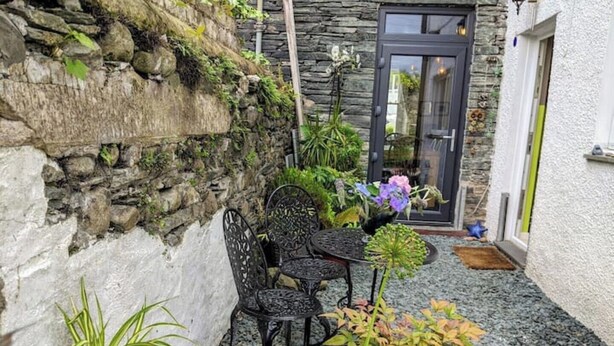 Un mur de pierre, une porte et une petite terrasse avec une table et des chaises.