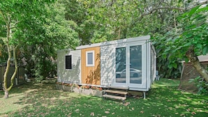 Eine kleine, einstöckige Holzhütte mit Holztür und großen Fenstern, umgeben von einem gepflegten Rasen und Bäumen.