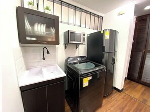 Compact kitchen with washing machine and microwave, featuring a tiled backsplash and dark cabinet.