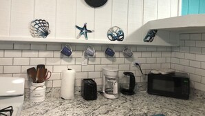 Una cocina con salpicadero de azulejos blancos, un reloj y diversos utensilios y electrodomésticos.