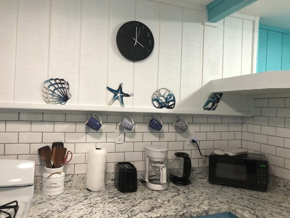 A kitchen with white tiled backsplash, a clock, and various kitchen utensils and appliances. - Tropic Cove Studio: 2 Bedroom unit, Wi-Fi, Air Conditioned, Centrally Located! (Mangrove Bush Settlement)