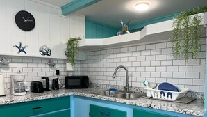 Una cocina con gabinetes color turquesa, un salpicadero de azulejos blancos, un microondas negro, una cafetera y un fregadero con un escurreplatos.