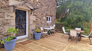 Ein Gebäude aus Stein mit einer Holzterrasse, Sitzgelegenheiten im Freien und Kübelpflanzen.