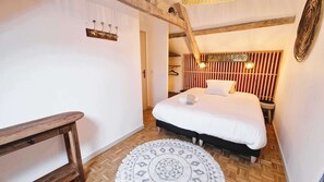 Ein Schlafzimmer mit einem hölzernen Bett, einem Nachttisch, einem Kleiderhaken und einem gemusterten Teppich.