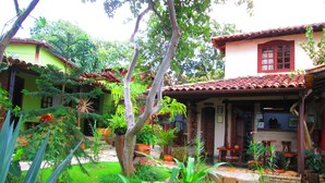 A lush garden with a variety of plants and trees, a patio area with outdoor seating, and a building with a red-tiled roof and a porch. - Pousada Bothanica (Pirenópolis)