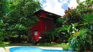 A red building with a swimming pool surrounded by lush greenery and a waterfall. - Pousada Bothanica (Pirenópolis)