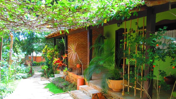 A stone pathway leading to a brick house with a green door, surrounded by lush greenery and various potted plants. - Pousada Bothanica (Pirenópolis)