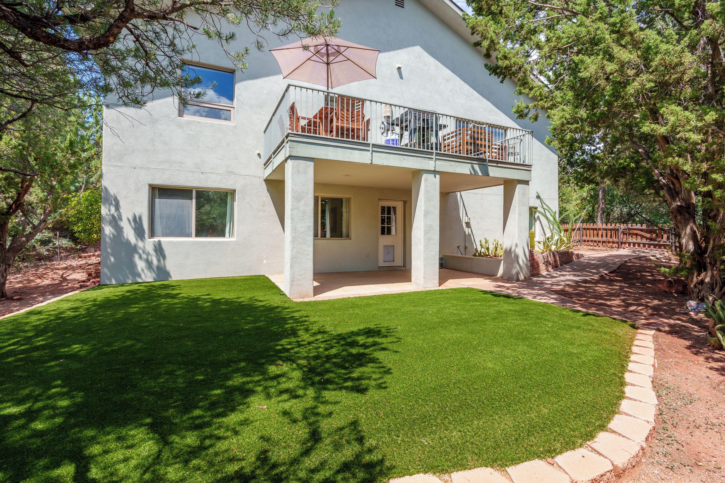 A modern two-story house with a balcony, a well-maintained lawn, and a brick pathway leading to the entrance.