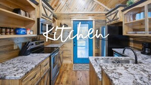 A kitchen with wooden walls, a blue door, granite countertops, and built-in shelves. - Private Couples' Retreat Near Beavers Bend (Broken Bow)