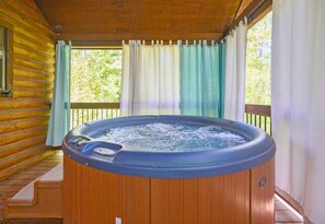 Un bain à remous dans un chalet en bois, doté d’une terrasse en bois et d’une fenêtre avec des rideaux.