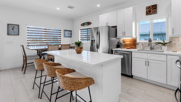 A modern kitchen with white cabinetry, a stainless steel refrigerator, and a central island with bar stools. - Snowbird Paradise - New Vacation Home in Key Largo (Key Largo)