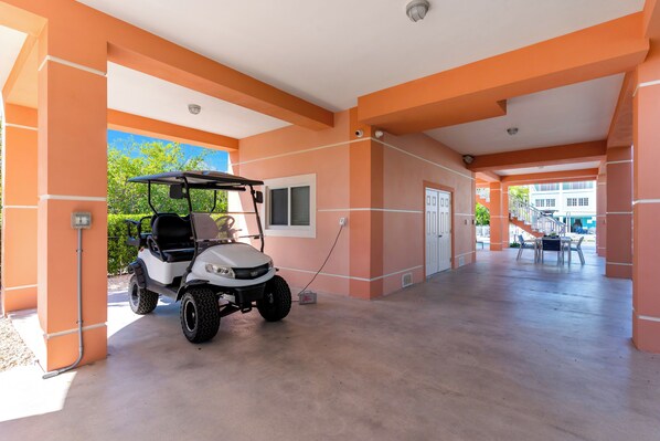 A covered parking area with a golf cart, orange walls, and a clear view of the outside. - Snowbird Paradise - New Vacation Home in Key Largo (Key Largo)