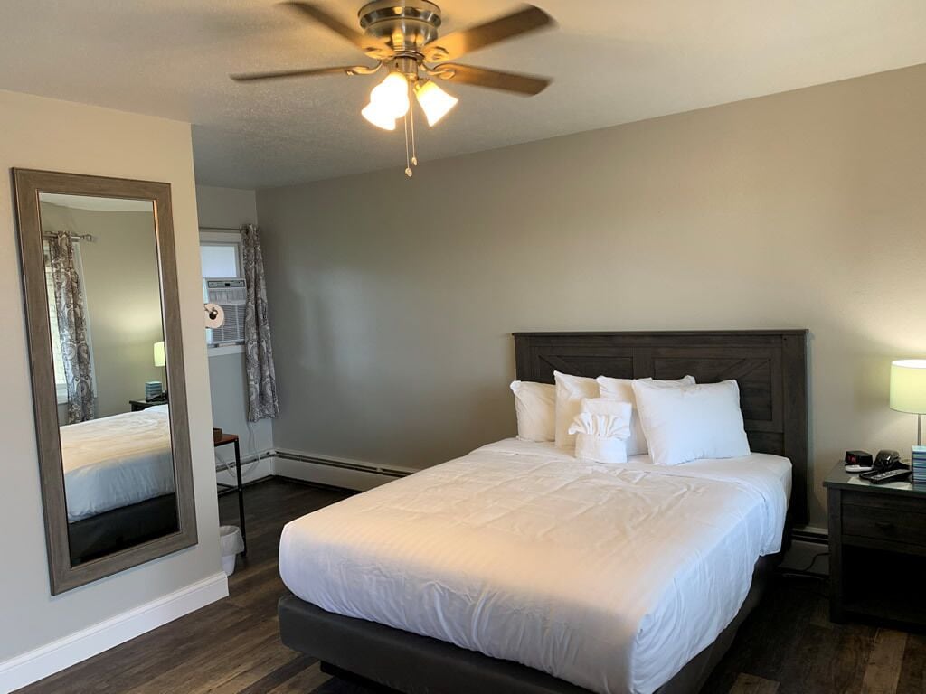 A hotel room with a bed, a ceiling fan, a nightstand, and a mirror.