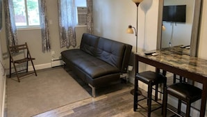A living room with a black leather sofa, a wooden chair, a small table with two stools, a floor lamp, and a large mirror. - Lakeside Motel (Ashland)