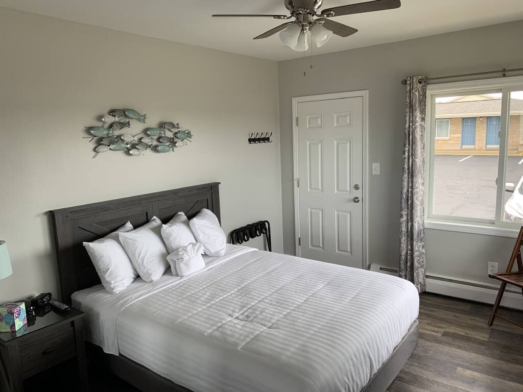 A bedroom with a bed, a nightstand, a ceiling fan, a door, and a window with curtains.