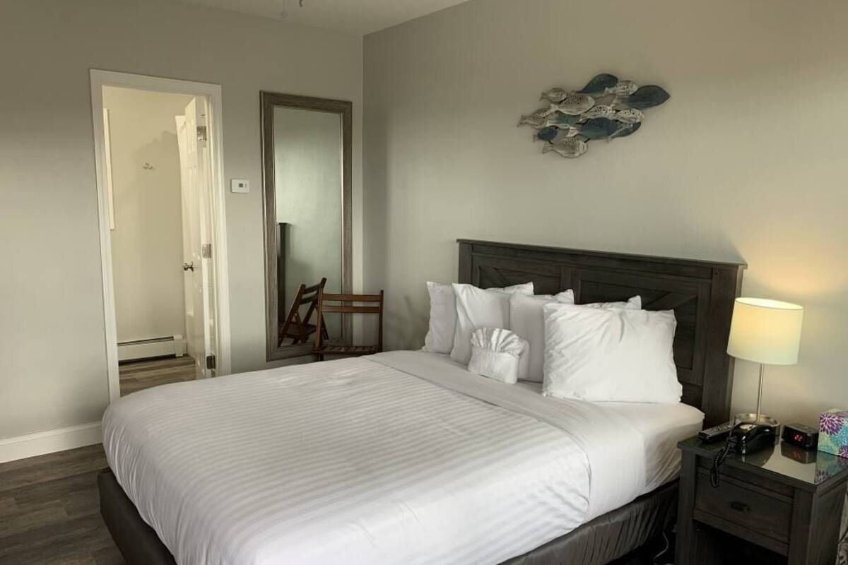 A neatly made bed with white linens, a dark wooden headboard, a bedside lamp, and a small table with a phone and a clock.