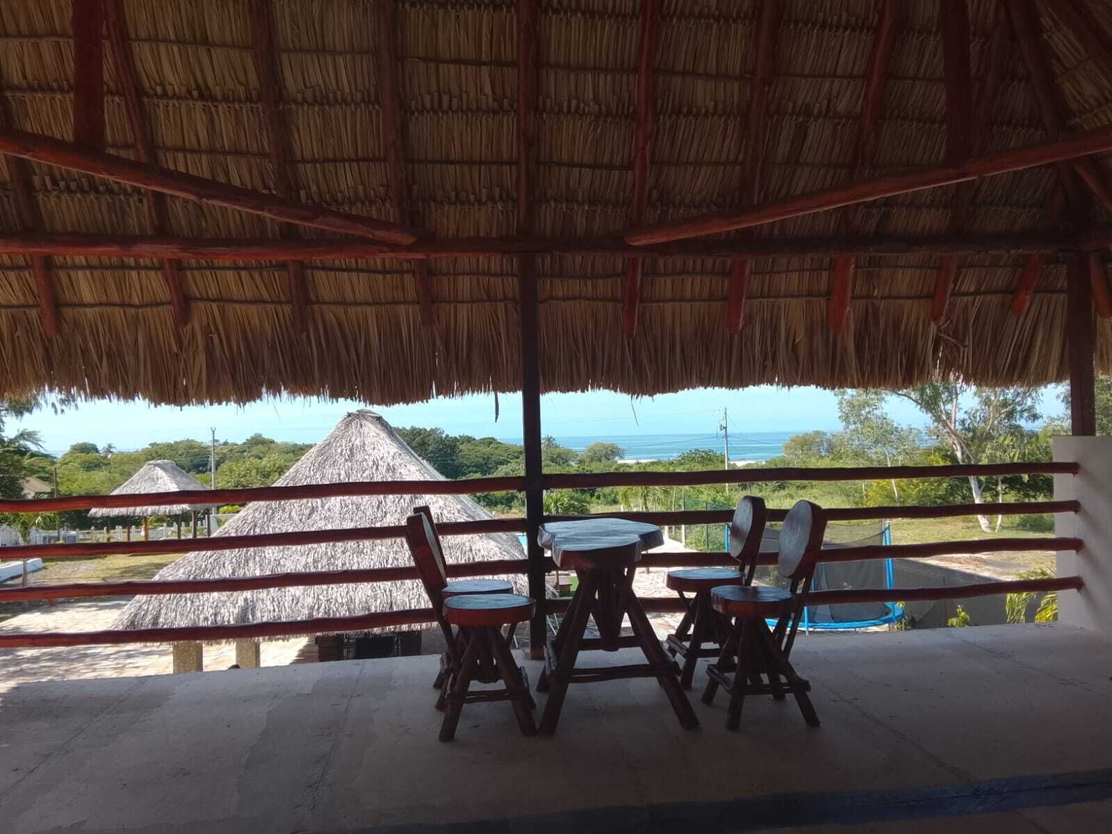 Ein Sitzbereich im Freien mit einem Reetdach, mit Blick auf einen Strand mit Gebäuden mit Reetdächern und eine Meerblick.