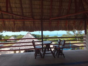 An outdoor seating area with a thatched roof, overlooking a beach with thatched-roof buildings and a view of the ocean. - Private Beach Villa w/ Pool • 5 Bedrooms • Sleeps 14 (El Velero)