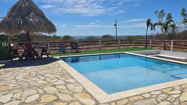 A swimming pool with stone tiles, a thatched umbrella, and a view of the sea. - Private Beach Villa w/ Pool • 5 Bedrooms • Sleeps 14 (El Velero)