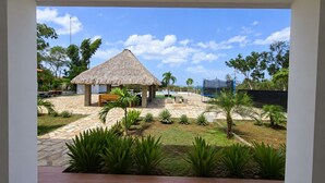 A courtyard with a thatched-roof structure, palm trees, and a stone pathway. - Private Beach Villa w/ Pool • 5 Bedrooms • Sleeps 14 (El Velero)