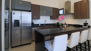 Una cocina moderna con electrodomésticos de acero inoxidable, armarios de madera oscura y una isla central con taburetes de bar.