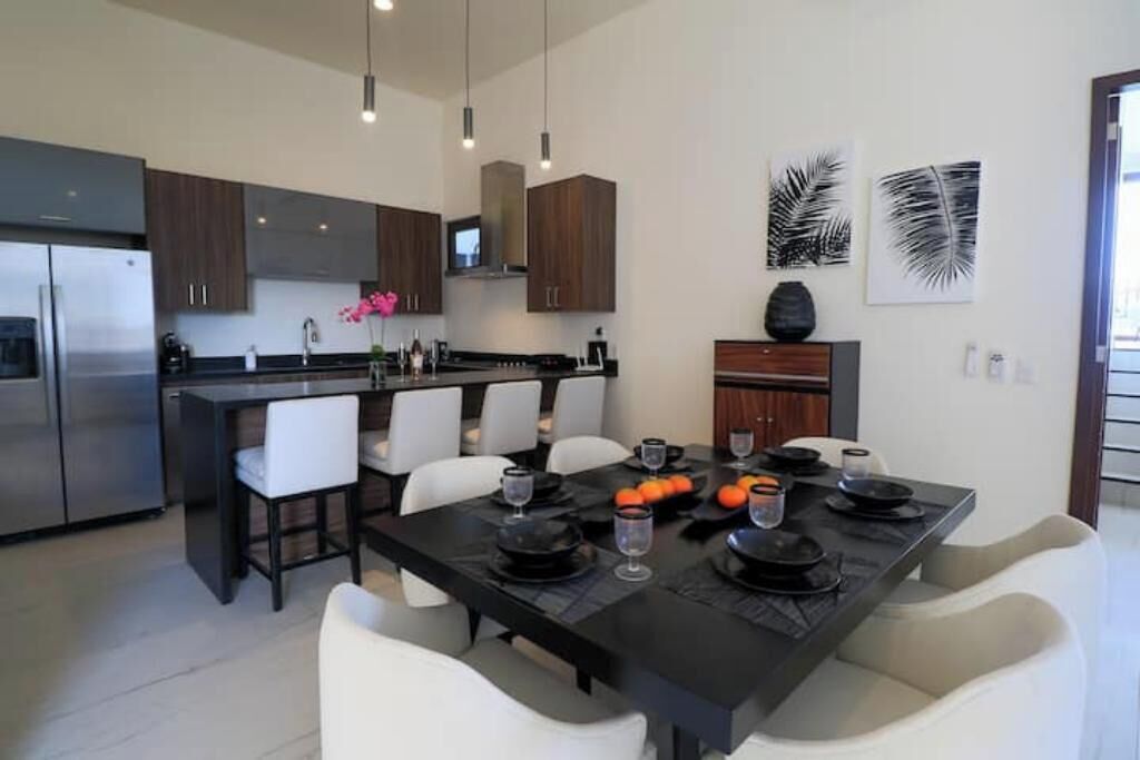 A modern kitchen with a central island, white chairs, and a dining table set for four.