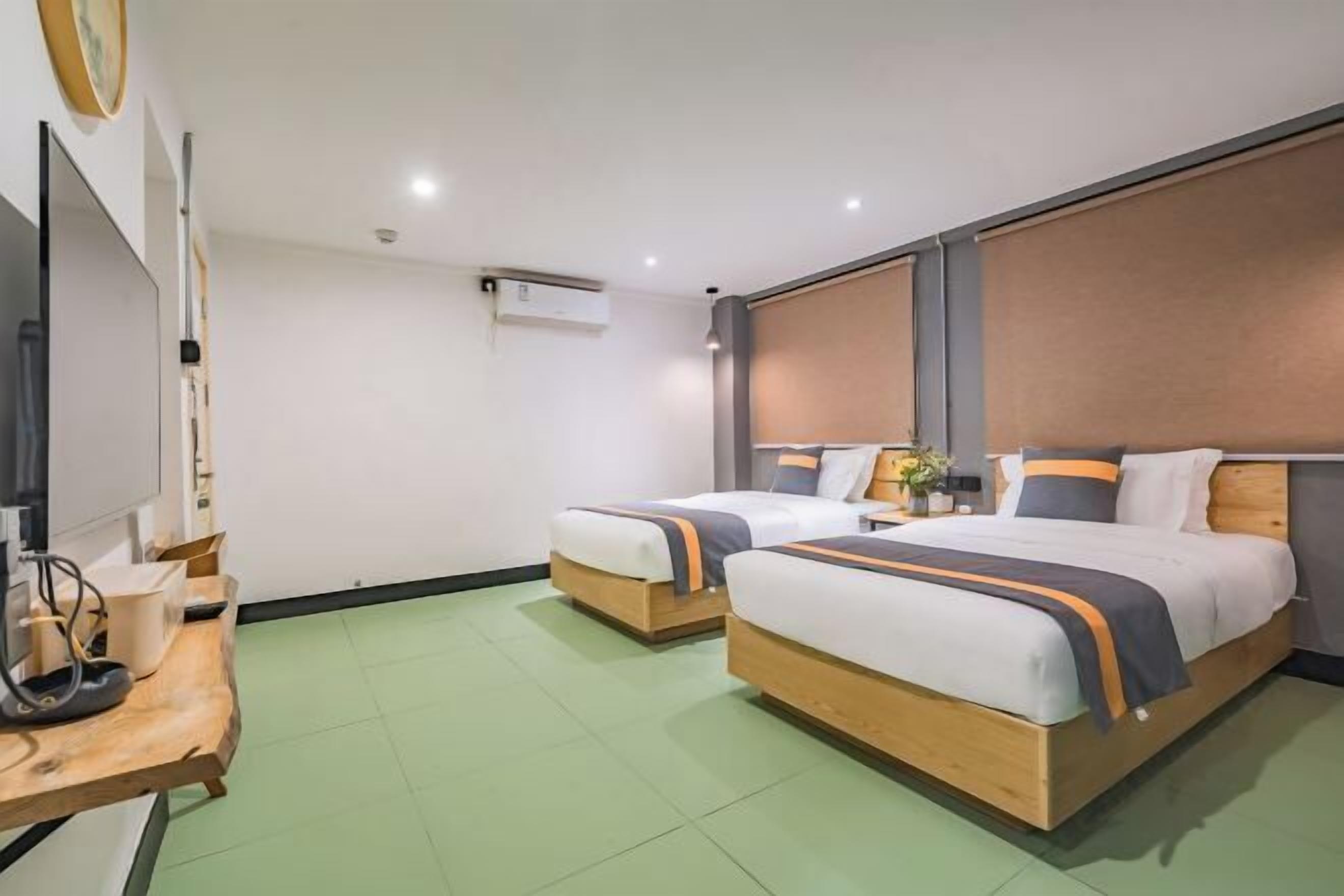 A hotel room with two beds, a wooden desk, a flat-screen TV, and a large window.