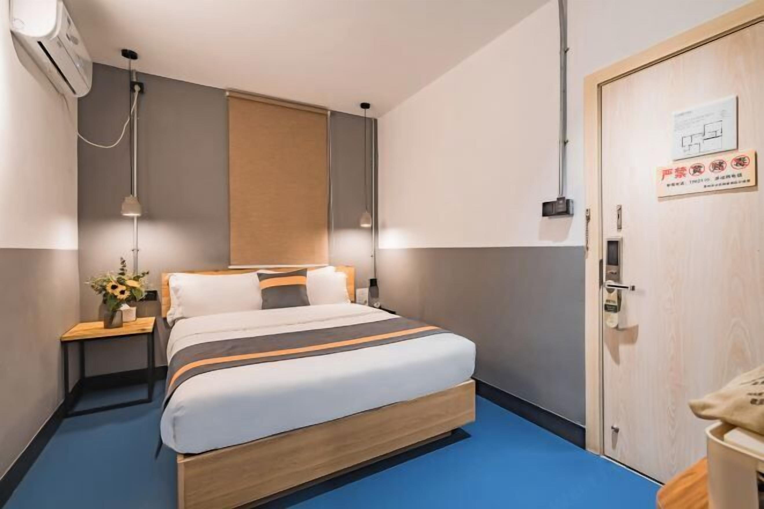 Una habitación de hotel con cama, mesita de noche, lámpara y una puerta con un cartel.