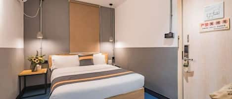 Una habitación de hotel con cama, mesita de noche, lámpara y una puerta con un cartel.