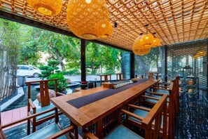 A restaurant with a long wooden table and chairs, a woven ceiling, and a view of greenery outside. - Xihu Yingxiu Xinsu Guesthouse (Huizhou)