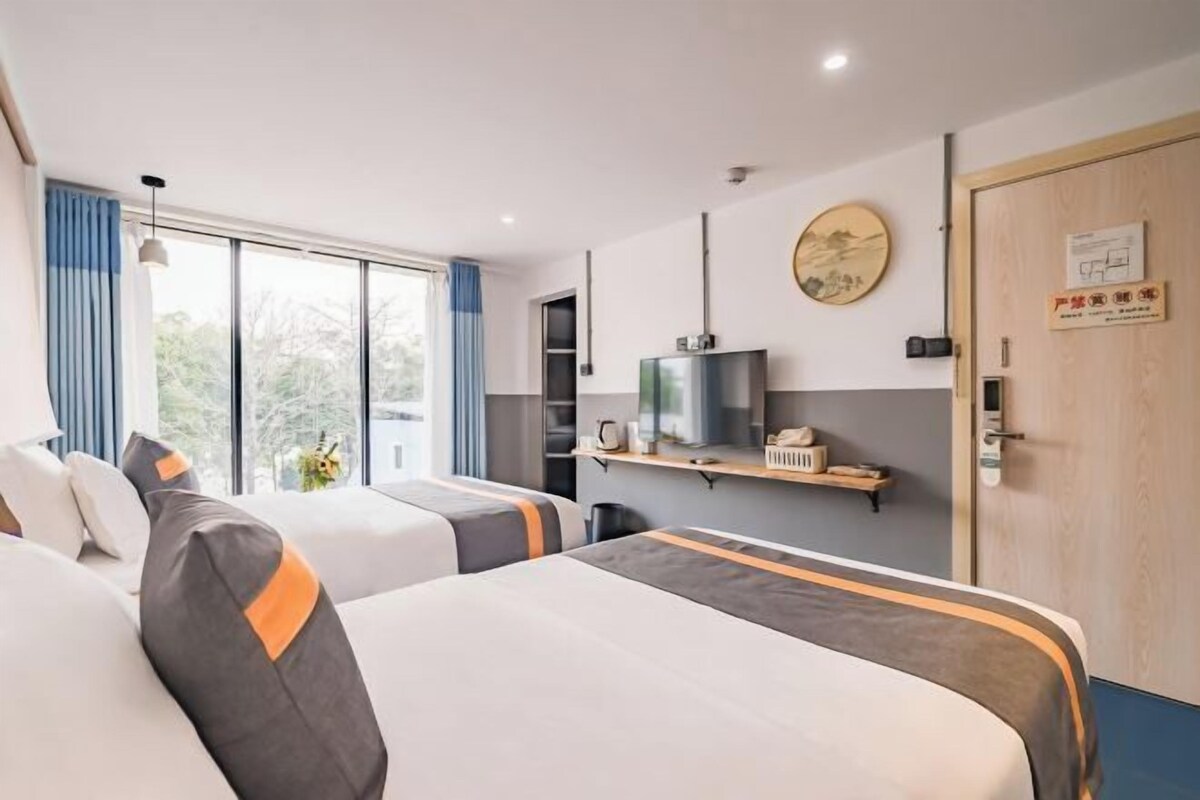 A hotel room with two beds, a television, a shelf with items, and a door with a sign.