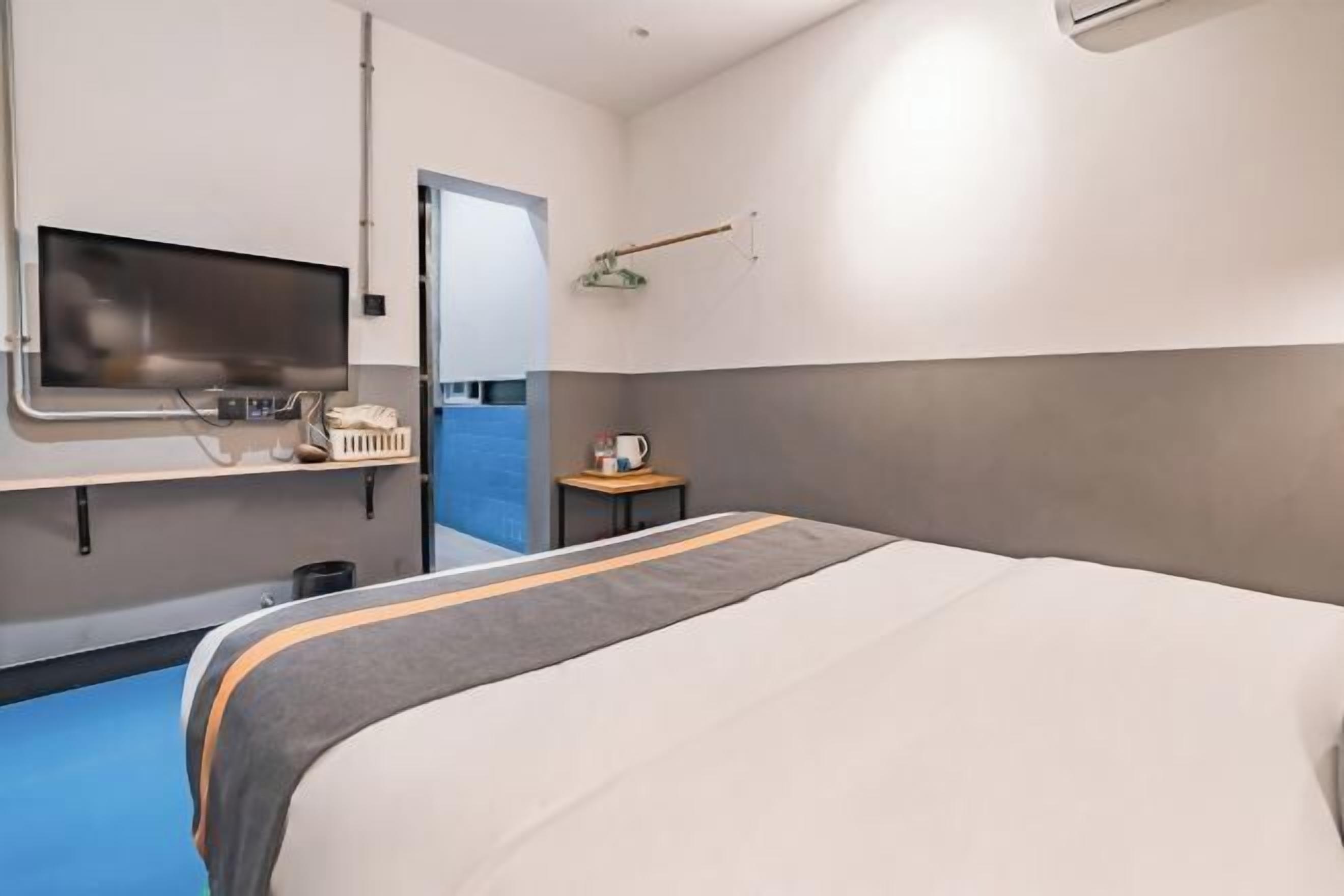 Ein Hotelzimmer mit Bett, Fernseher, einem kleinen Tisch mit Wasserkocher und Blick auf einen blauen Außenbereich.