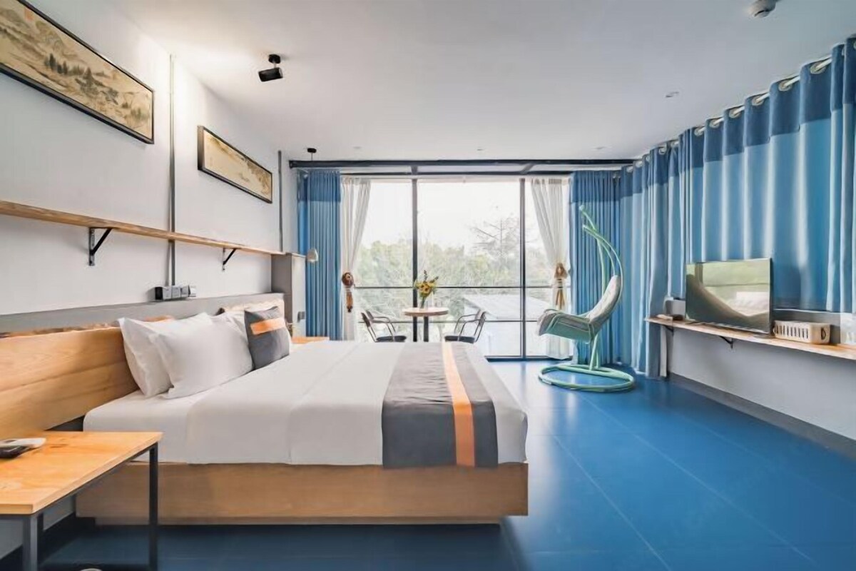 A modern hotel room with a large bed, a desk, a chair, and a TV.